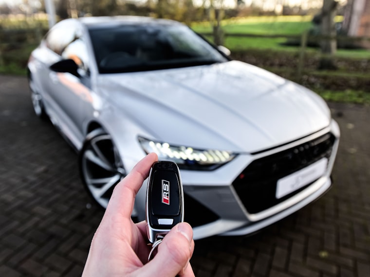 A hand pressing a remote in front of a white car with its lights on