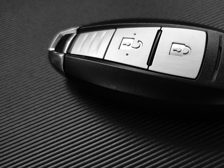 A black smart key fob with lock and unlock buttons resting on a dark carbon-textured surface