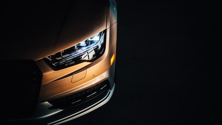 Amber-lit headlight and fender of a modern car against black