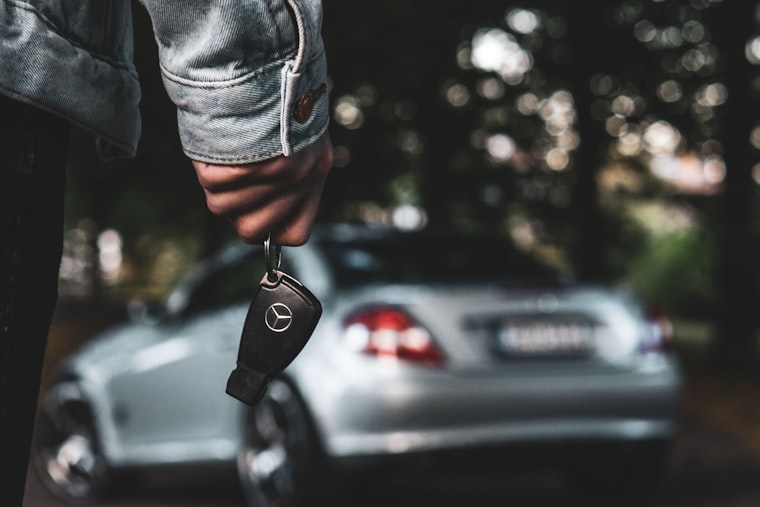 A hand holding a car key at night, parked cars blurred behind it